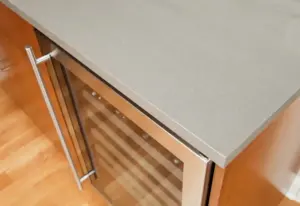 A grey quartz countertop over a wooden cabinet and beverage refrigerator in a Springville, UT kitchen