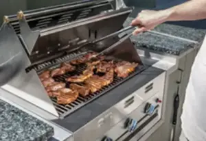 A man grilling chicken on a barbecue built into a granite countertop in an outdoor kitchen in Springville, UT.